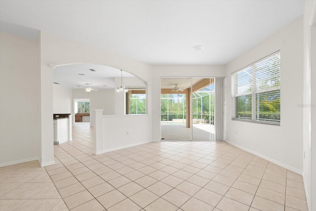 unfurnished room with arched walkways, light tile patterned flooring, and a ceiling fan