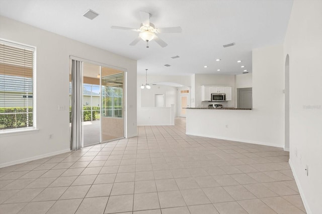 unfurnished living room featuring arched walkways, visible vents, ceiling fan, and baseboards