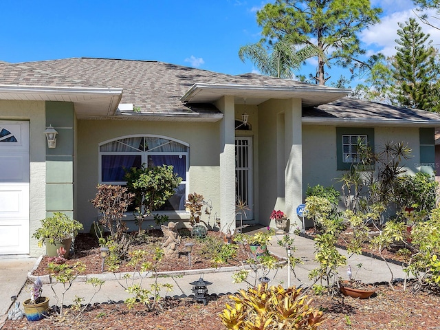 entrance to property featuring a garage, roof with shingles, and stucco siding