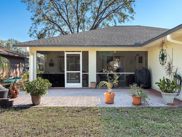 back of house featuring a sunroom, roof with shingles, a patio, and stucco siding