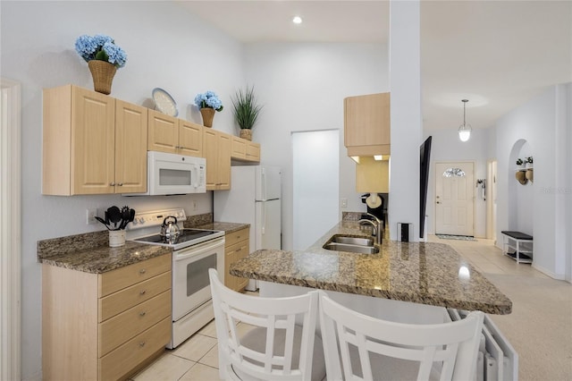 kitchen featuring light brown cabinetry, a breakfast bar area, a peninsula, white appliances, and a sink