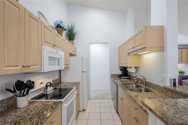 kitchen with a sink, dark stone counters, white appliances, and light brown cabinets