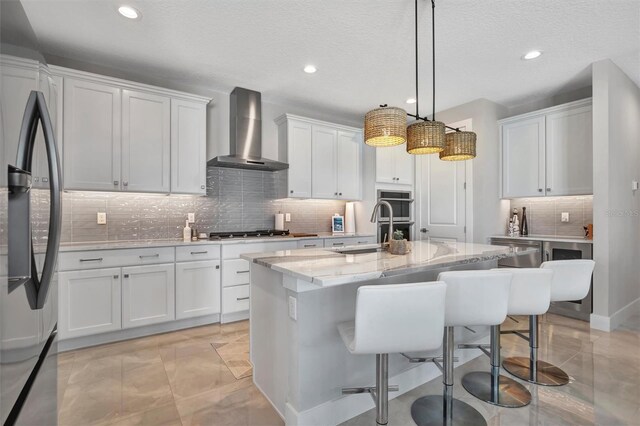 6027 White Mangrove Ln, Bradenton, FL 34210 - kitchen with an island with sink, a kitchen breakfast bar, appliances with stainless steel finishes, wall chimney exhaust hood, and white cabinets