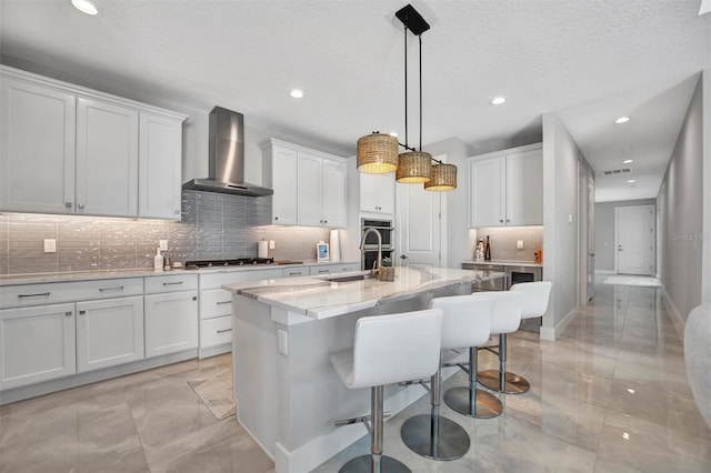 6027 White Mangrove Ln, Bradenton, FL 34210 - kitchen featuring an island with sink, a sink, white cabinetry, appliances with stainless steel finishes, and wall chimney exhaust hood