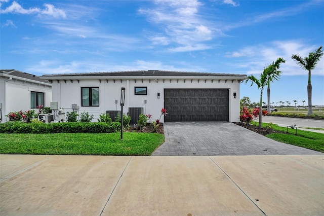 view of front facade with stucco siding, cooling unit, decorative driveway, and a garage