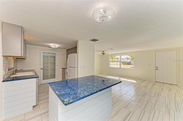 kitchen with visible vents, open floor plan, freestanding refrigerator, a ceiling fan, and a sink