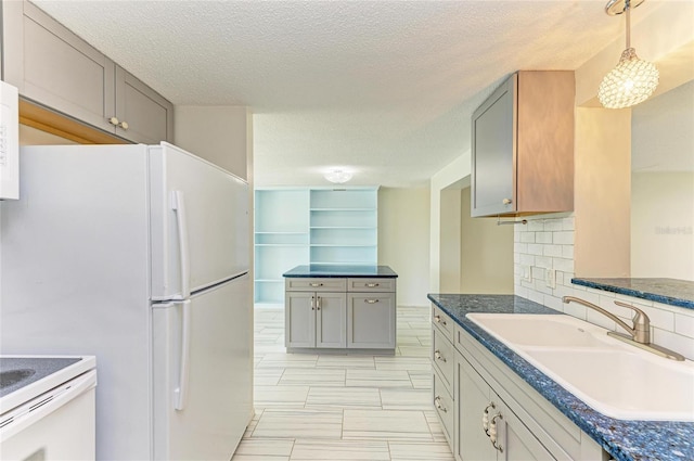 kitchen featuring freestanding refrigerator, a sink, decorative backsplash, pendant lighting, and dark countertops