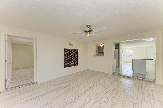 unfurnished room with visible vents, a textured ceiling, and ceiling fan