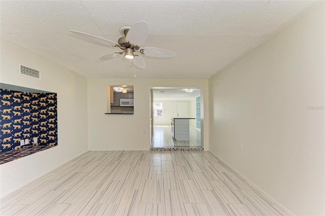 unfurnished room with a ceiling fan, visible vents, and a textured ceiling