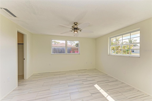 empty room featuring a ceiling fan, visible vents, a wealth of natural light, and a textured ceiling