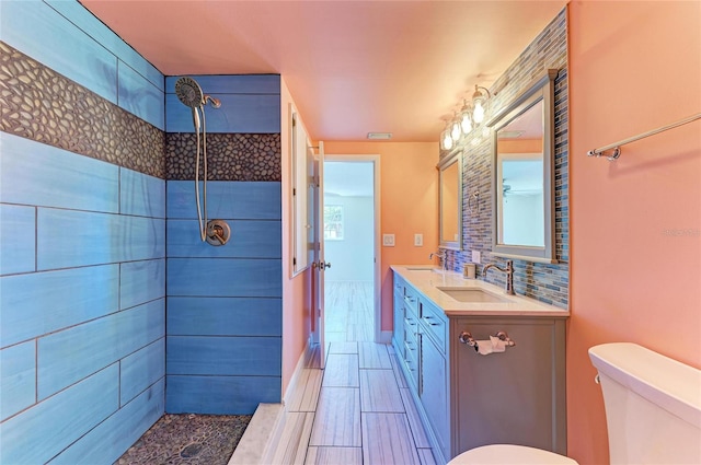 bathroom featuring tiled shower, double vanity, a sink, toilet, and backsplash