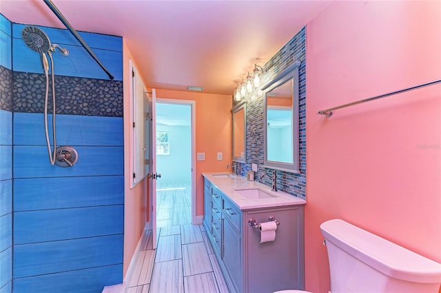 bathroom with toilet, tiled shower, tasteful backsplash, and a sink