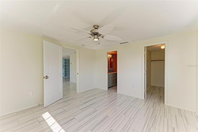 unfurnished bedroom featuring visible vents, a walk in closet, a closet, a textured ceiling, and a ceiling fan