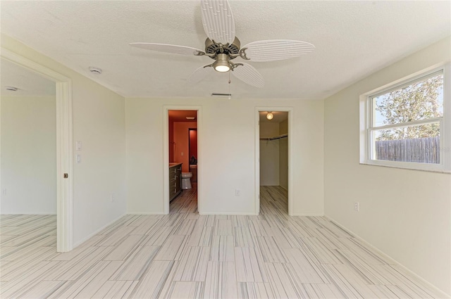 unfurnished bedroom featuring a spacious closet, a closet, ensuite bath, a textured ceiling, and a ceiling fan