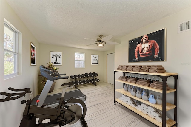 exercise area featuring ceiling fan, visible vents, light wood finished floors, and a textured ceiling