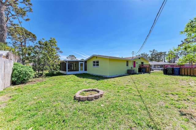 rear view of property featuring central air condition unit, stucco siding, a lawn, fence, and a sunroom