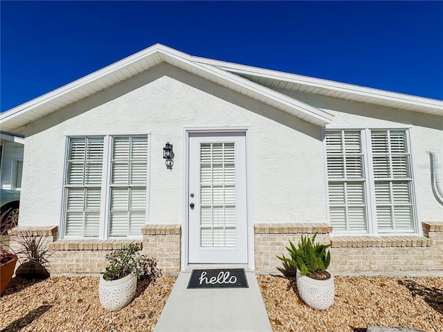 view of exterior entry featuring brick siding and stucco siding