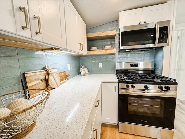 kitchen with light stone counters, stainless steel appliances, lofted ceiling, tasteful backsplash, and white cabinets