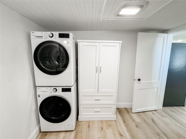 washroom featuring light wood-type flooring, stacked washing maching and dryer, baseboards, and cabinet space