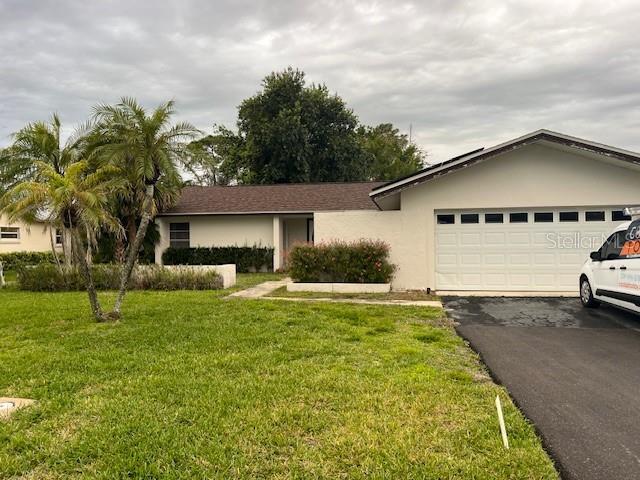 single story home with aphalt driveway, an attached garage, a front lawn, and stucco siding