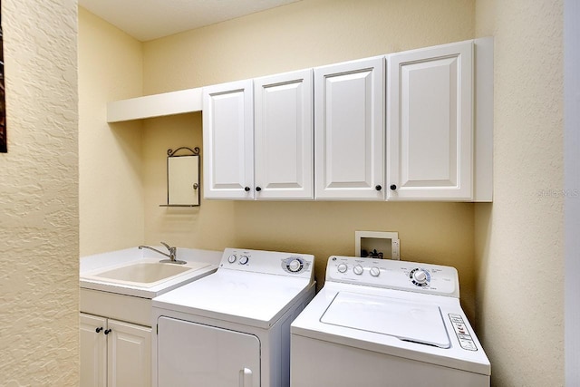 clothes washing area with cabinet space, washer and dryer, a textured wall, and a sink