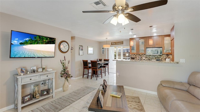 living area with light tile patterned floors, ceiling fan, visible vents, and baseboards