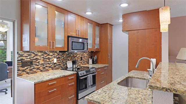 kitchen featuring stainless steel appliances, a sink, decorative backsplash, light stone countertops, and brown cabinetry