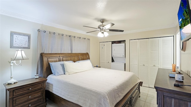 bedroom featuring light tile patterned floors, stacked washer / dryer, ceiling fan, crown molding, and two closets