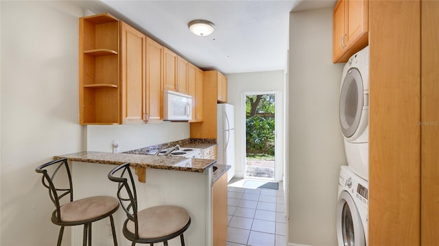 kitchen featuring light tile patterned floors, white appliances, a breakfast bar, open shelves, and stacked washer and clothes dryer