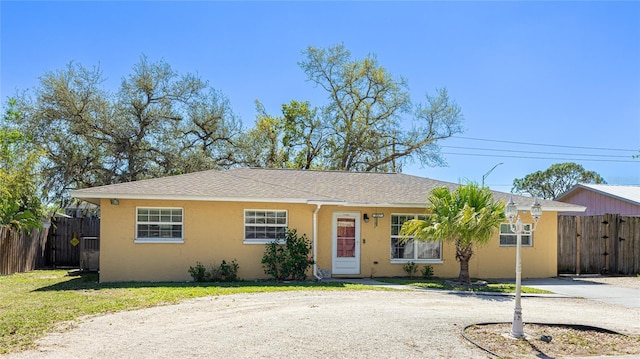 ranch-style home with driveway, a front yard, fence, and stucco siding