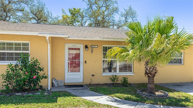 property entrance featuring roof with shingles and stucco siding