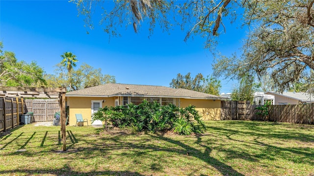 rear view of property featuring a lawn, a fenced backyard, and stucco siding