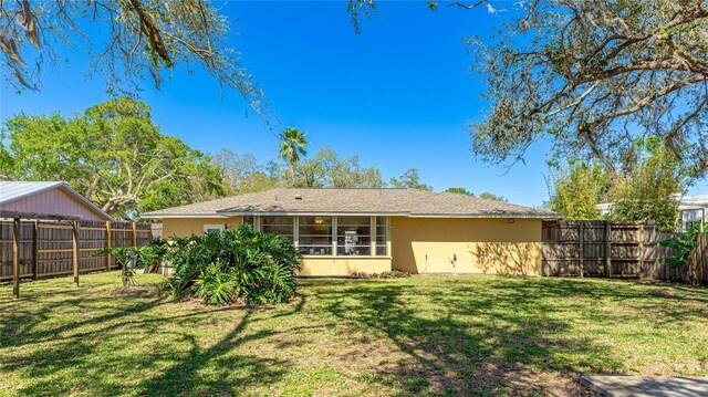 back of house featuring a yard, a fenced backyard, a sunroom, and stucco siding