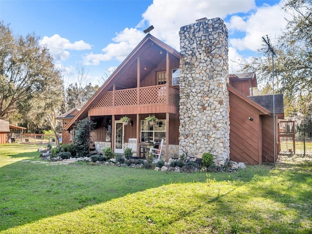 view of front of house with a shingled roof, a balcony, stone siding, a chimney, and a front lawn