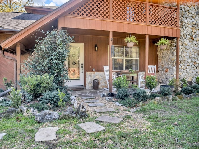 property entrance with stone siding, a shingled roof, and a porch