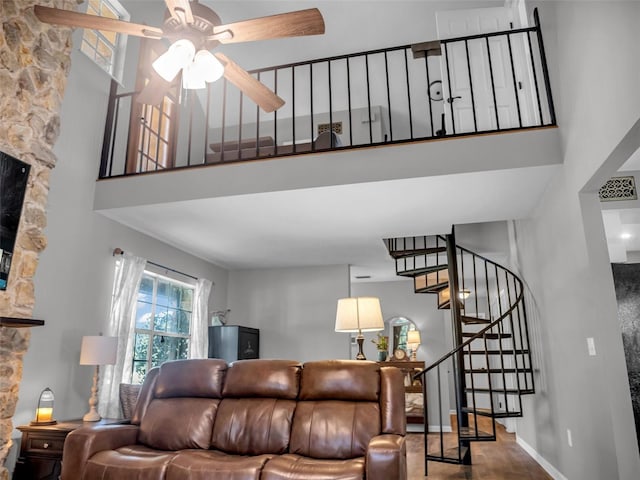 living room featuring a high ceiling, a ceiling fan, visible vents, baseboards, and stairway