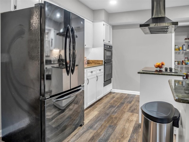 kitchen with dark wood finished floors, dark countertops, wall chimney exhaust hood, black appliances, and white cabinetry