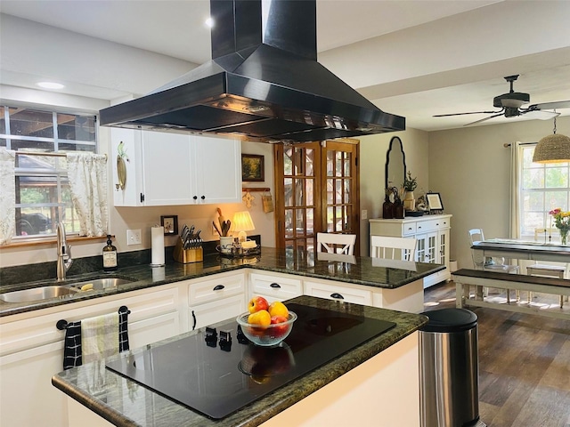 kitchen with island exhaust hood, white cabinetry, a sink, wood finished floors, and a peninsula