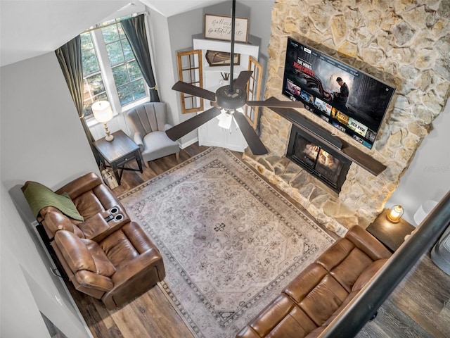 living room featuring vaulted ceiling, a stone fireplace, baseboards, and wood finished floors