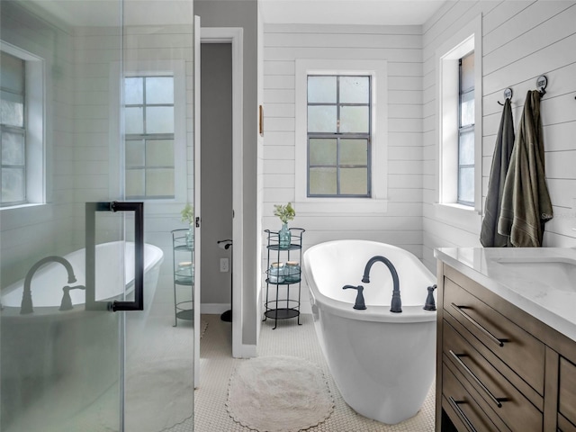 full bath with a soaking tub, tile patterned flooring, wood walls, and vanity