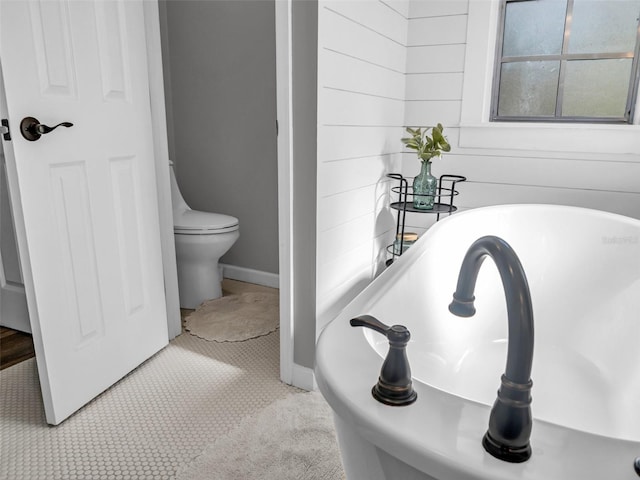 full bath with toilet, a soaking tub, and baseboards