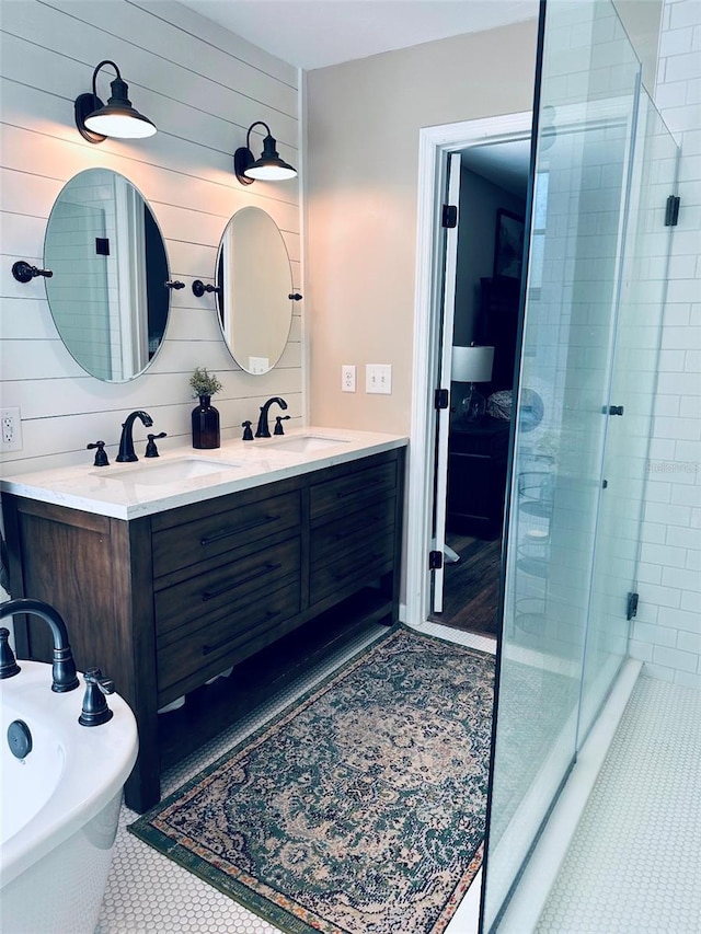 full bathroom with double vanity, tile patterned flooring, a tile shower, and a sink