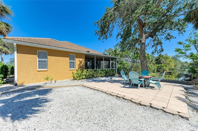 back of house with a tile roof, a sunroom, a patio area, and stucco siding