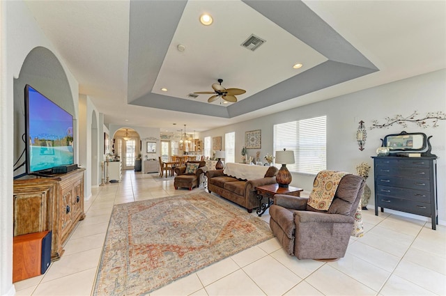 living room with arched walkways, a tray ceiling, light tile patterned flooring, and visible vents