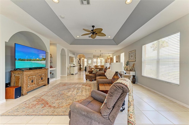 living room featuring arched walkways, recessed lighting, baseboards, tile patterned floors, and a tray ceiling