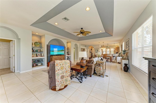 living room with built in shelves, a raised ceiling, baseboards, and light tile patterned floors