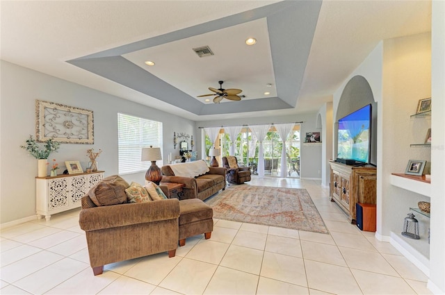 living room featuring a tray ceiling, light tile patterned floors, visible vents, ceiling fan, and baseboards