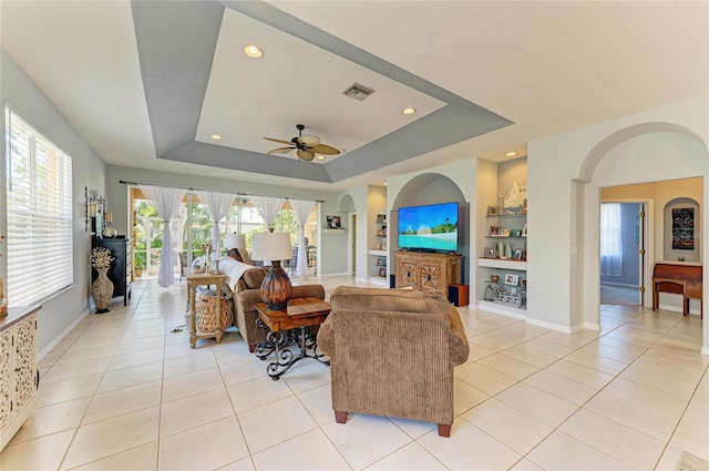 living room with light tile patterned floors, built in shelves, visible vents, and a raised ceiling