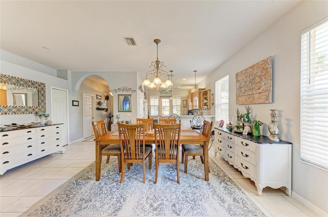 dining space featuring arched walkways, a notable chandelier, light tile patterned floors, visible vents, and baseboards