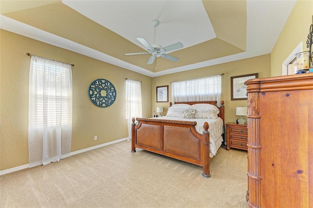 bedroom with multiple windows, baseboards, a raised ceiling, and light colored carpet